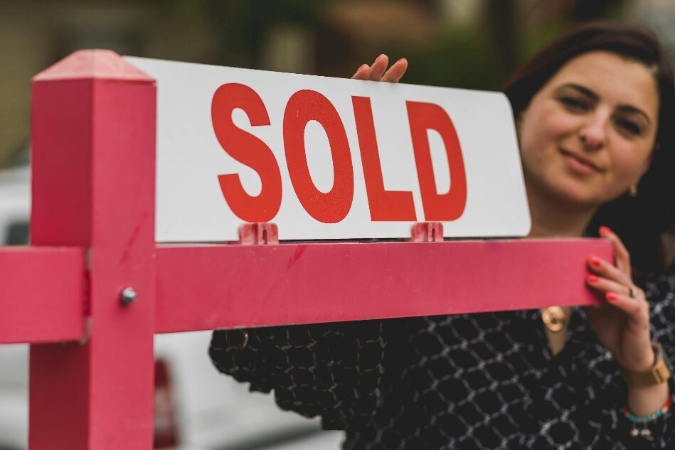 A woman next to a SOLD sign