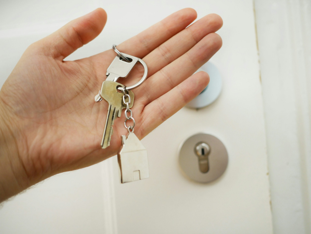 A hand holding a pair of keys with a house-shaped keychain