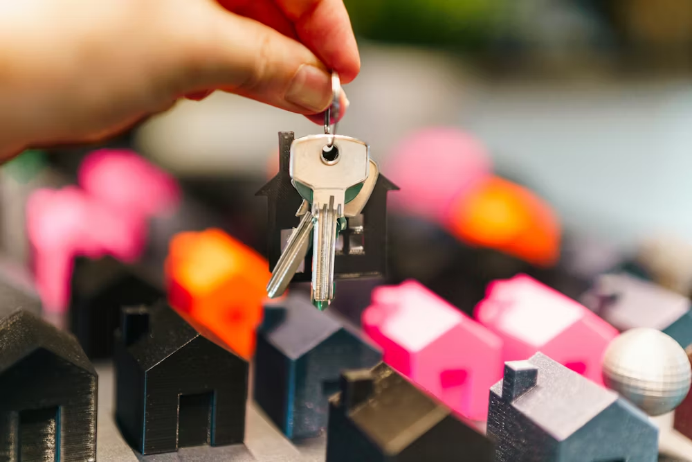 A person dangling a pair of keys over miniature houses