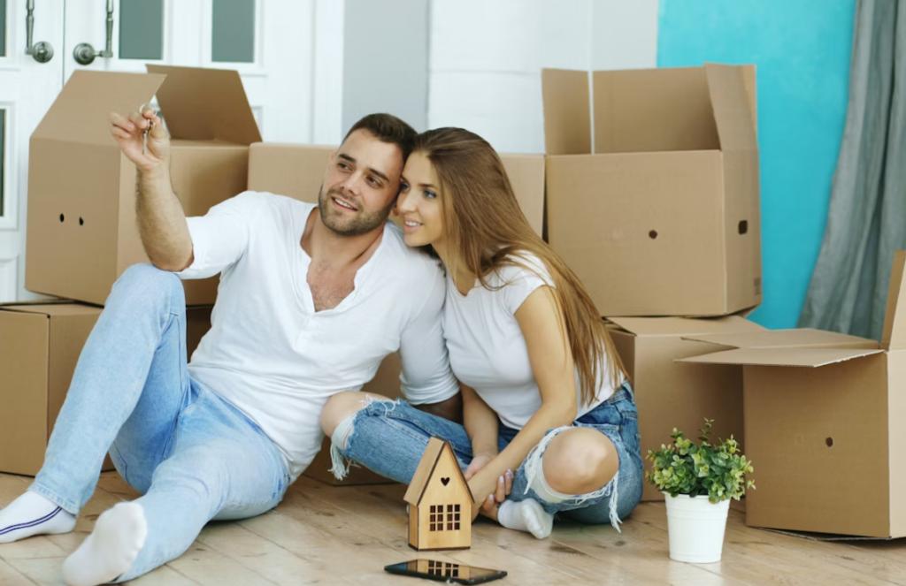 This image shows a happy couple sitting on floor with cartons in background.
