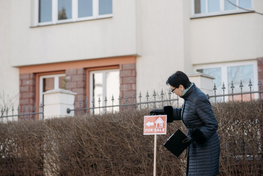 a realtor standing by a “for sale” sign outside a property