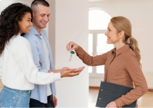 A real estate agent in a brown shirt hands house keys to a happy couple.