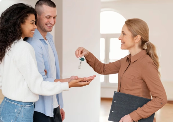 A real estate agent in a brown shirt hands house keys to a happy couple.